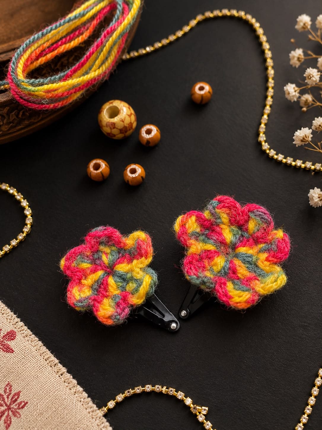 Two hand-crocheted flower clips in saffron, rose and sage wool, with wooden beads and a gold chain